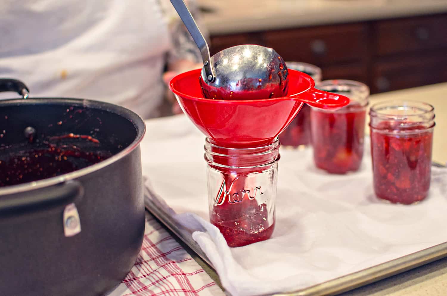 Canning fresh strawberry fig preserves by pouring into mason jars with funnel