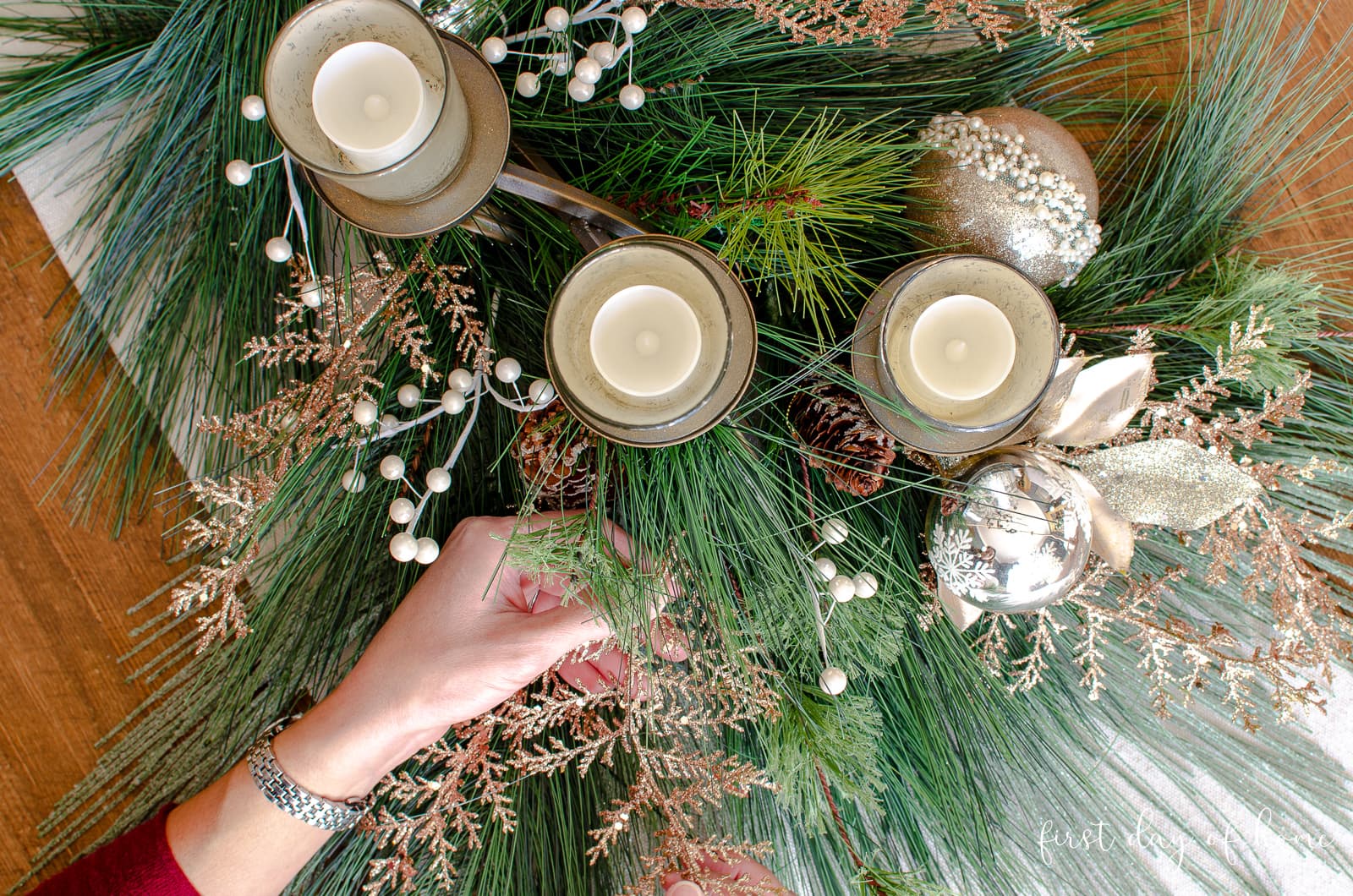 Placing metallic floral accents in DIY holiday centerpiece with mixed evergreens and mercury glass candleholders.