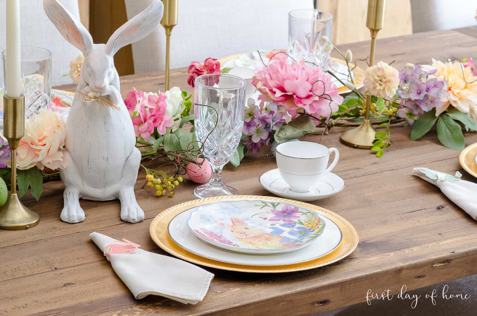 Easter place setting with gold chargers, bunny plate, bunny napkin rings and faux floral garland