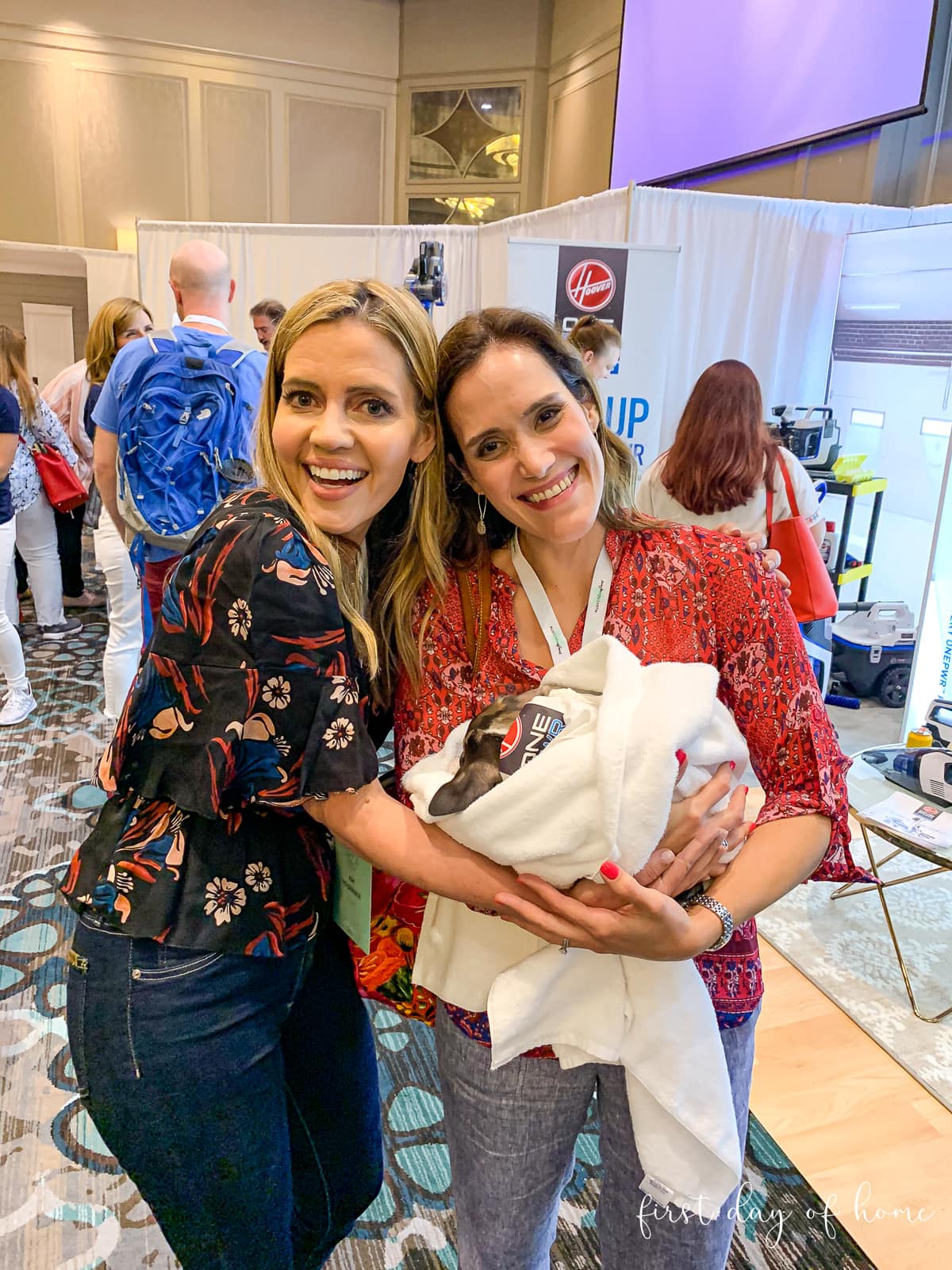 Kim Holderness and Crissy from First Day of Home holding a puppy at the Hoover booth at the Haven Conference
