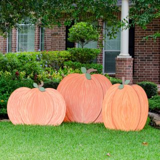 Three orange painted wooden pumpkins sitting on front yard as decorations for fall
