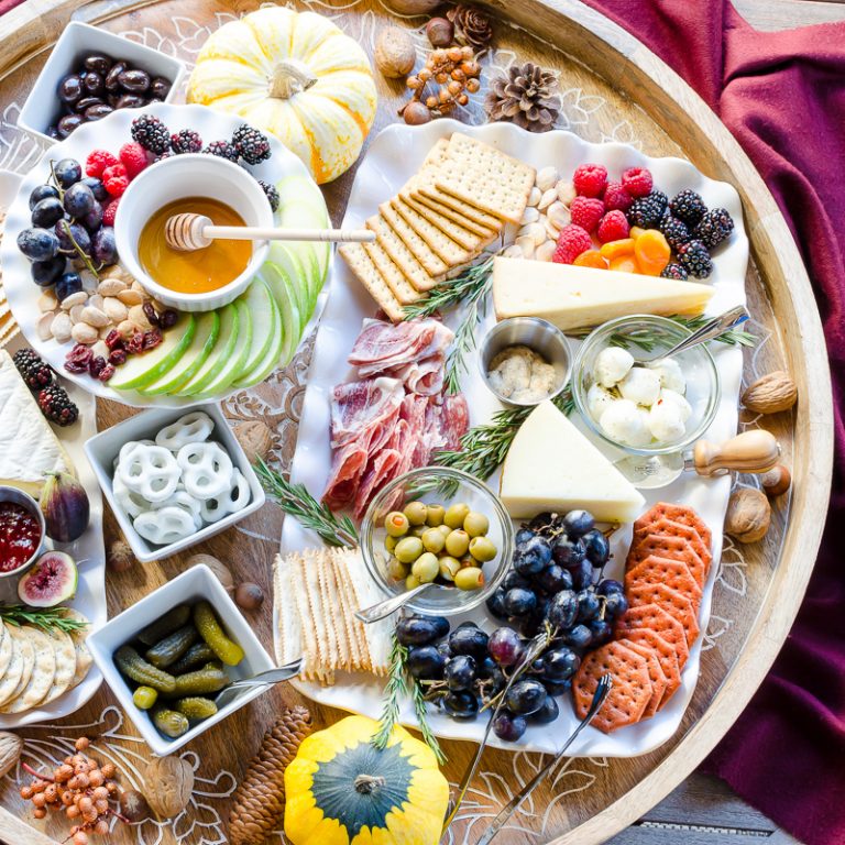 Charcuterie and cheese board with sweet and savory dishes, including cheeses, crackers, pretzels, olives, cornichons, and preserves