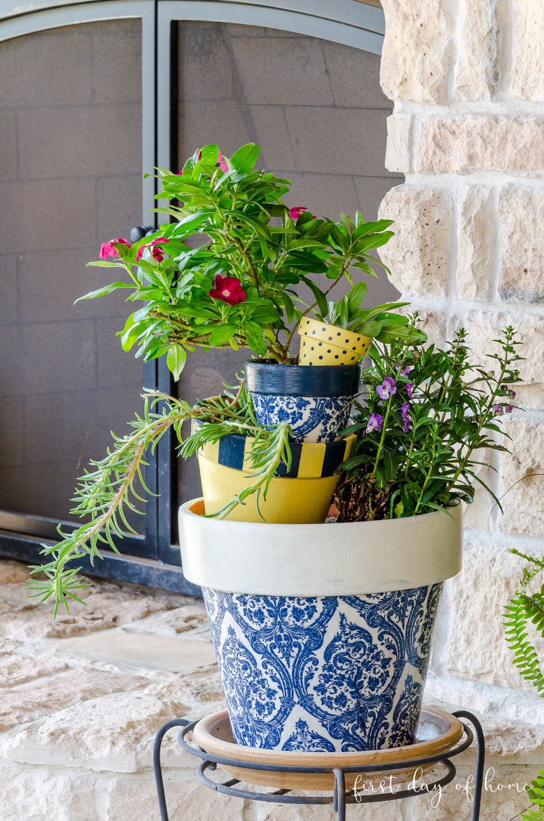 Decoupage stacked flower pots on plant stand by outdoor fireplace.