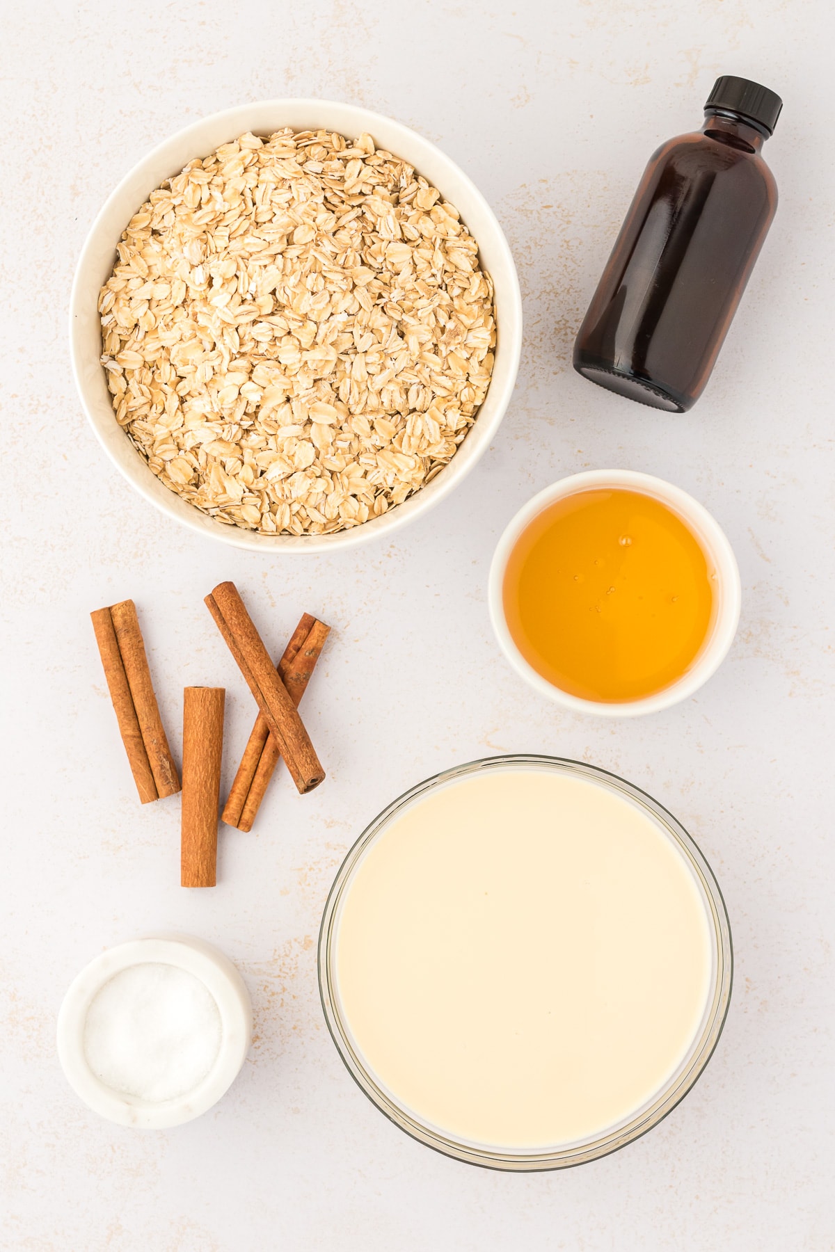 Ingredients for Mexican oatmeal breakfast, including old fashioned oats, cinnamon sticks, evaporated milk, honey, and vanilla with a dash of salt.