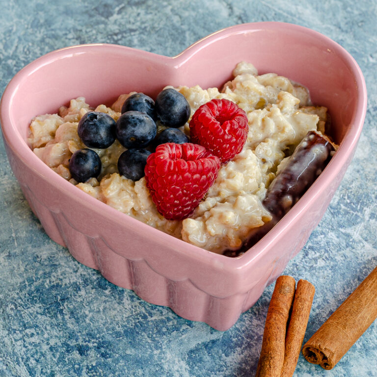 Mexican oatmeal (avena) in a heart shaped bowl topped with raspberries, blueberries and cinnamon sticks