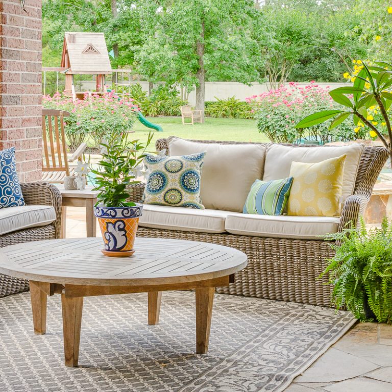 Outdoor decor with blue and yellow color scheme, teak furniture, woven outdoor seating and flowering plants