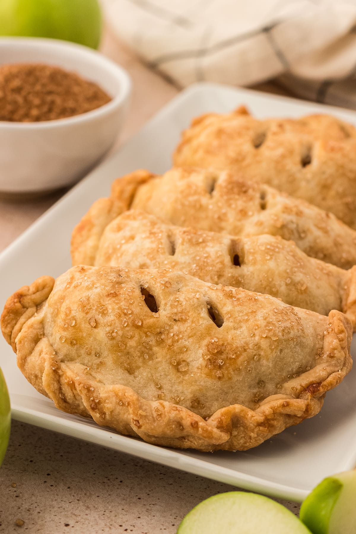 Apple empanadas sitting on a serving tray with green apples in the background