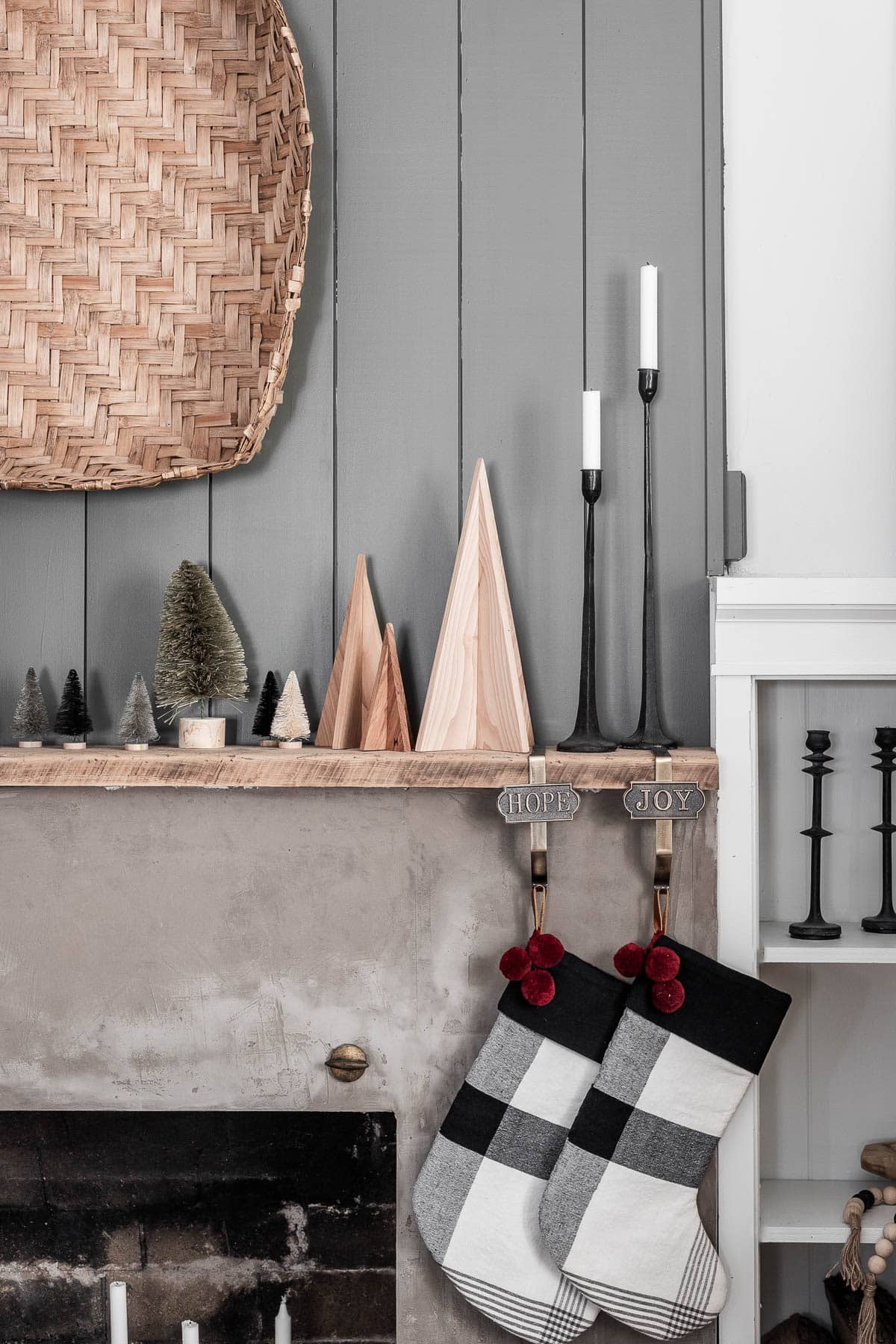 Scandinavian style minimalist Christmas mantel decor ideas with wooden trees, plaid stockings, and a basket hung above