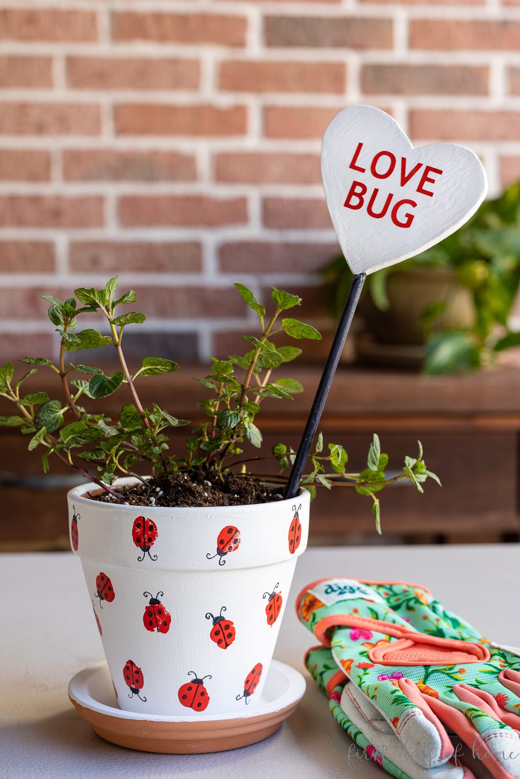 Flower pot with ladybug fingerprint design and garden stake reading "Love Bug" shown with gardening gloves.