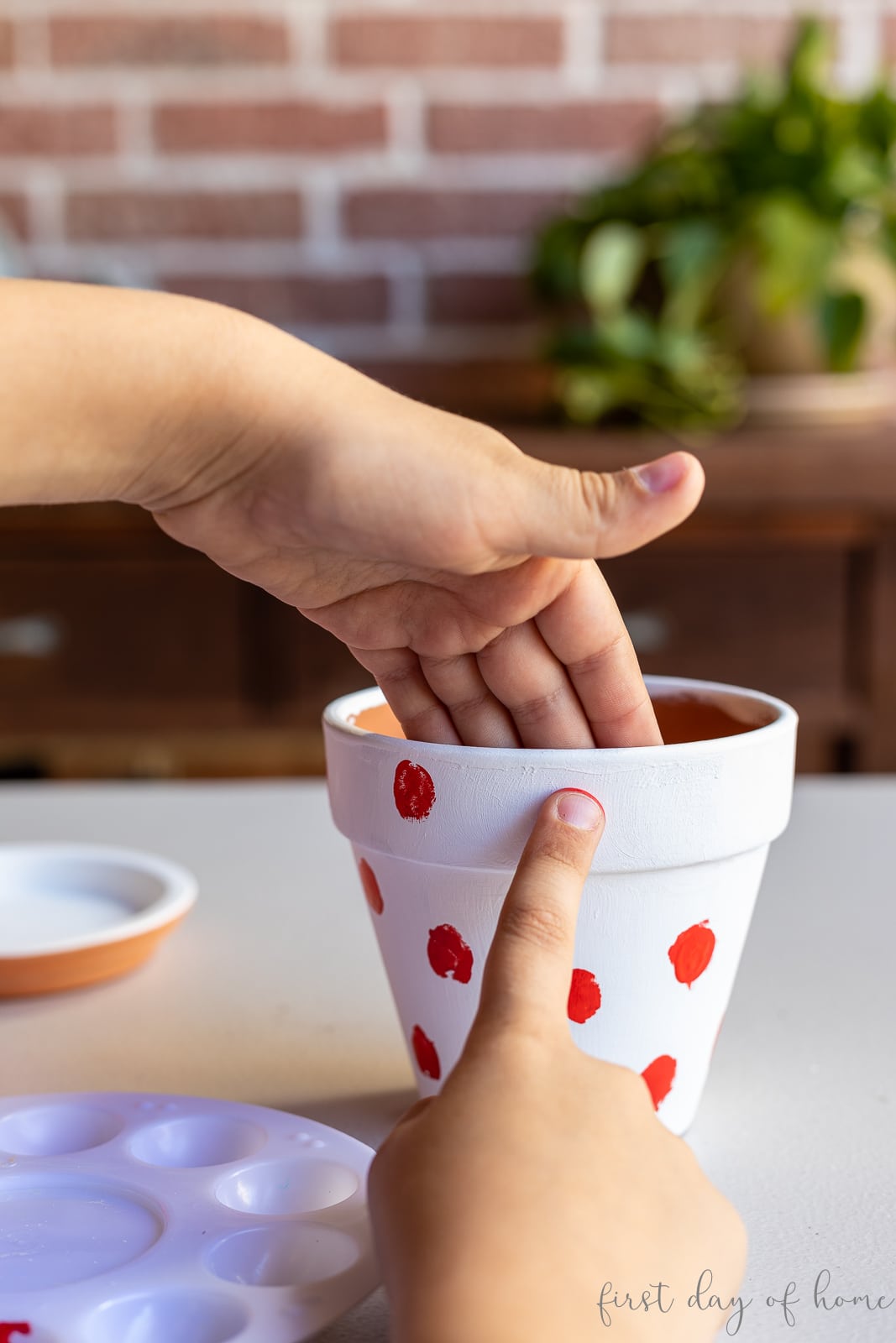 Child using fingerprint to paint flower pot with red dots to make ladybug design