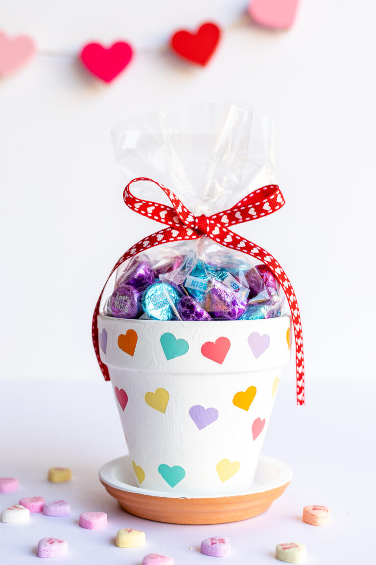 Valentines Day flower pot with colored hearts painted on it, surrounded by conversation hearts candies