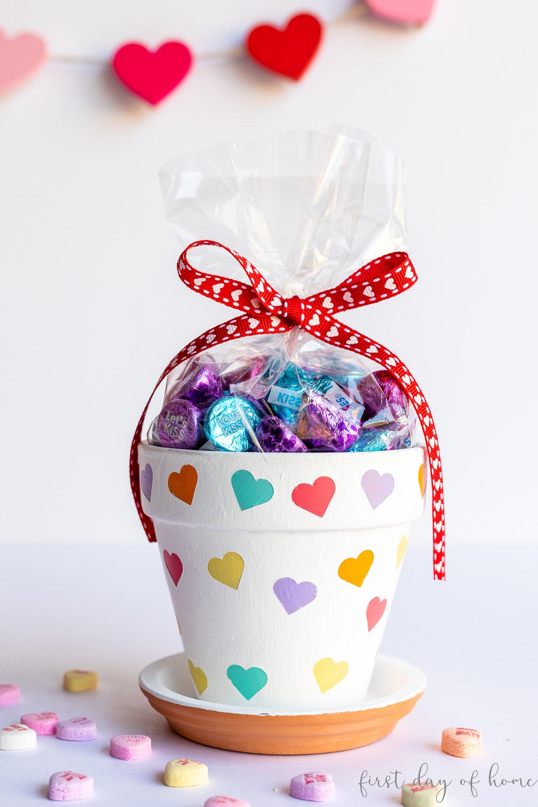 Valentines Day flower pots with colored hearts painted on it, filled with chocolates and with Valentine's Day candies surrounding it