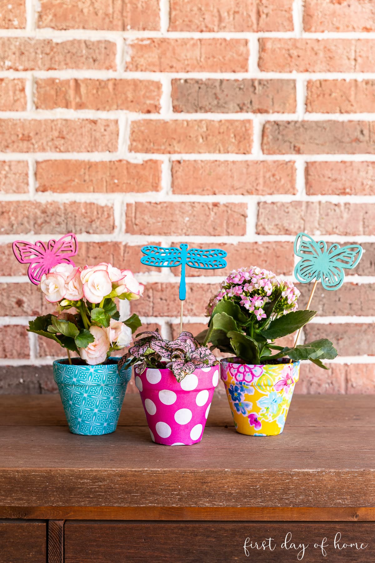 Trio of brightly colored fabric covered flower pots shown with DIY garden stakes in front of brick wall