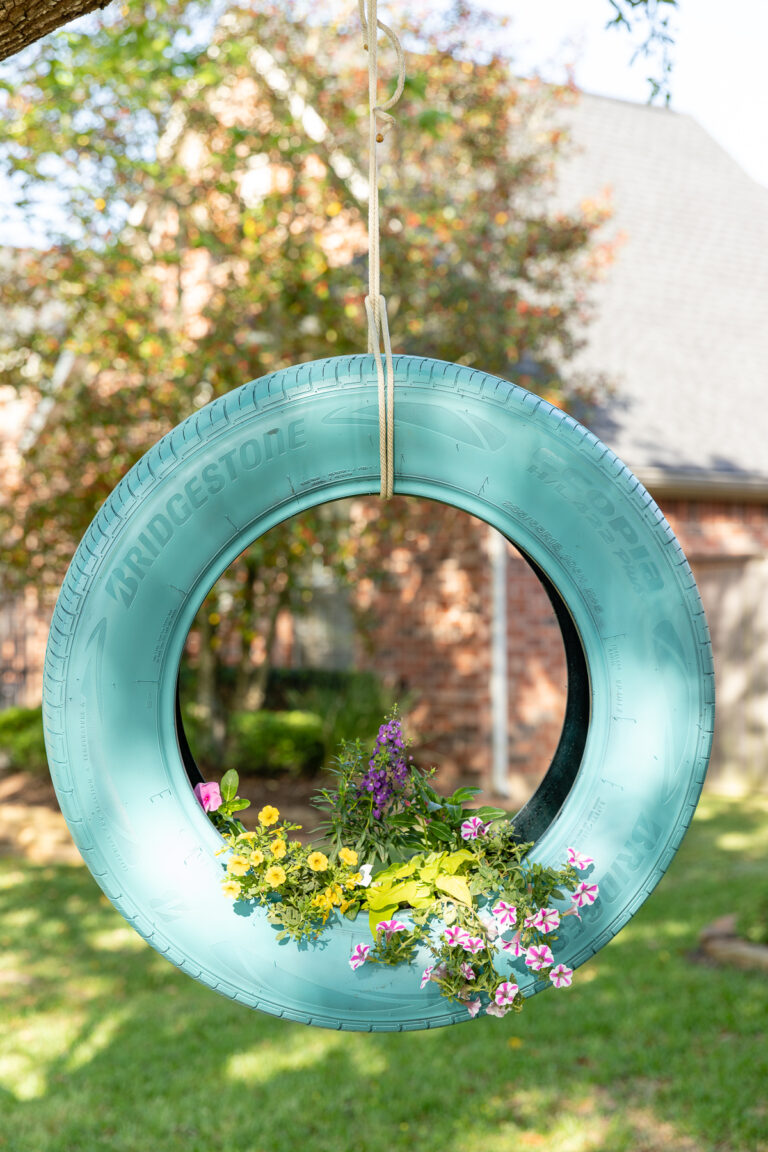 Spray painted tire planter with mixed floral container garden arrangement, hanging from a tree branch