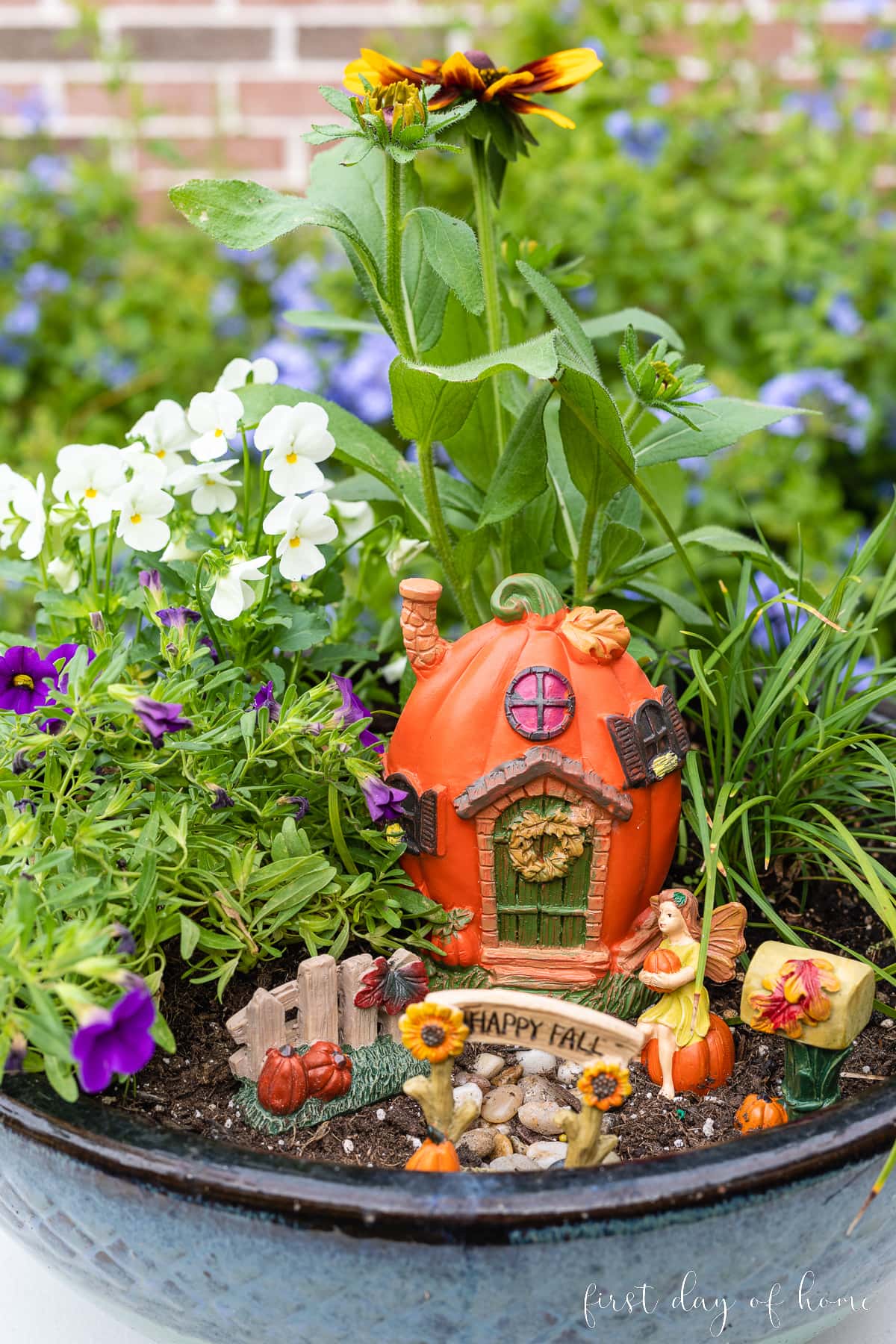 Fall fairy garden with figurines from Dollar Tree including a pumpkin house, fence, mailbox, and small fairy