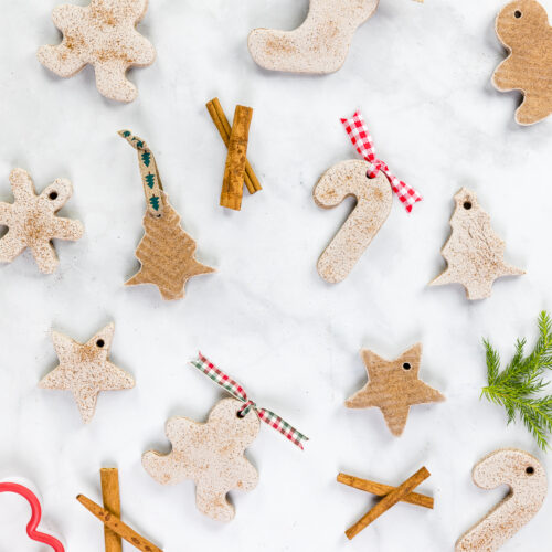 cinnamon salt dough ornaments in various Christmas shapes shown with cinnamon sticks and cookie cutters