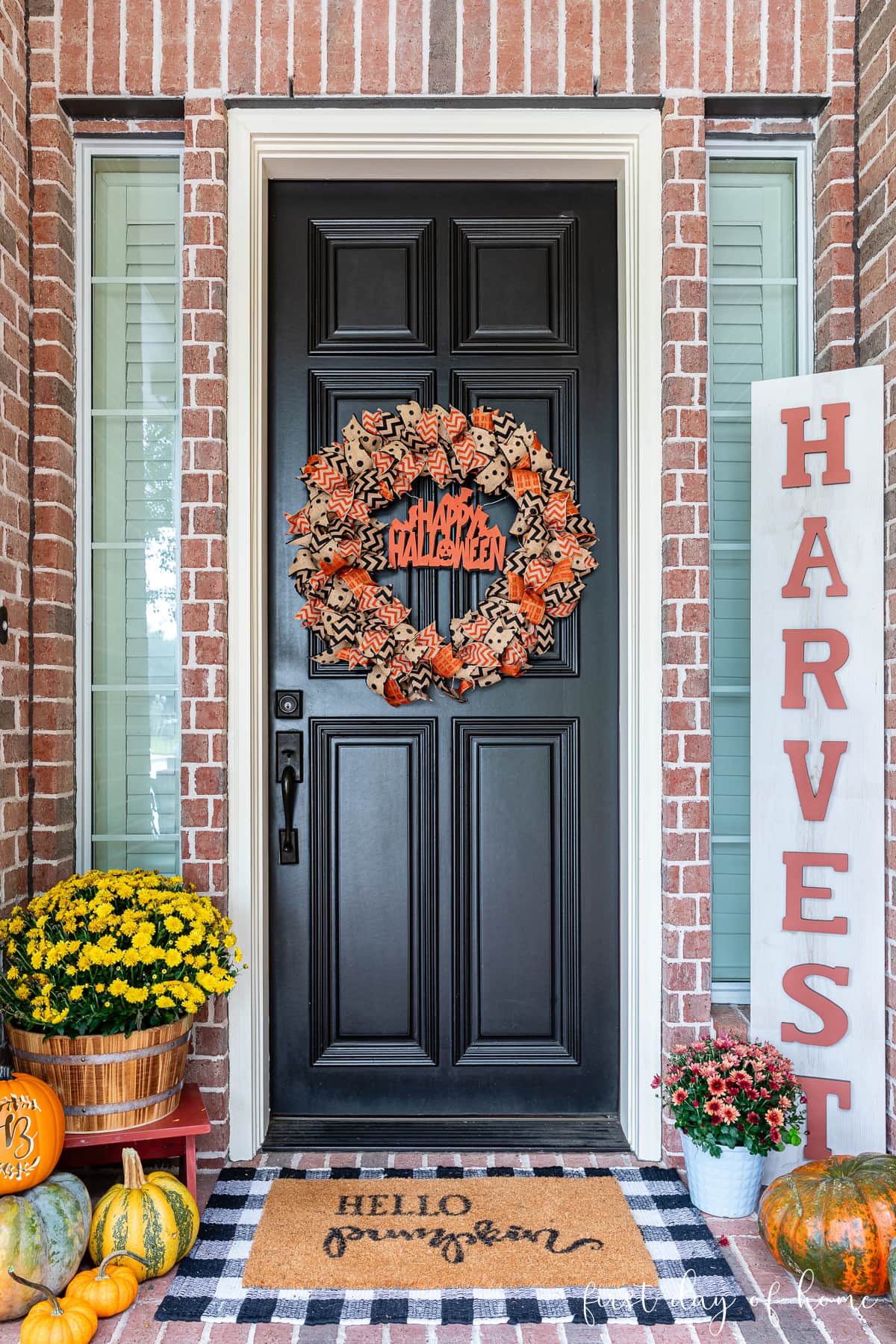 Front porch decorated for Halloween with rag wreath hanging on front door, mums, and pumpkins