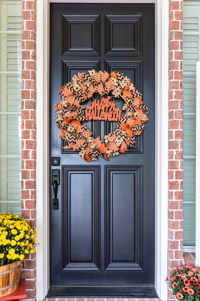DIY rag wreath with Halloween themed burlap ribbon hanging on front door with mums next to doorstep