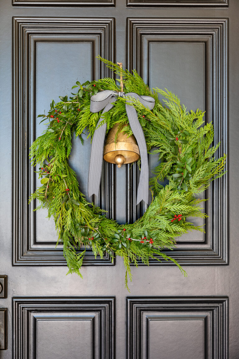 DIY winter wreath with bell and farmhouse ribbon hanging on front door