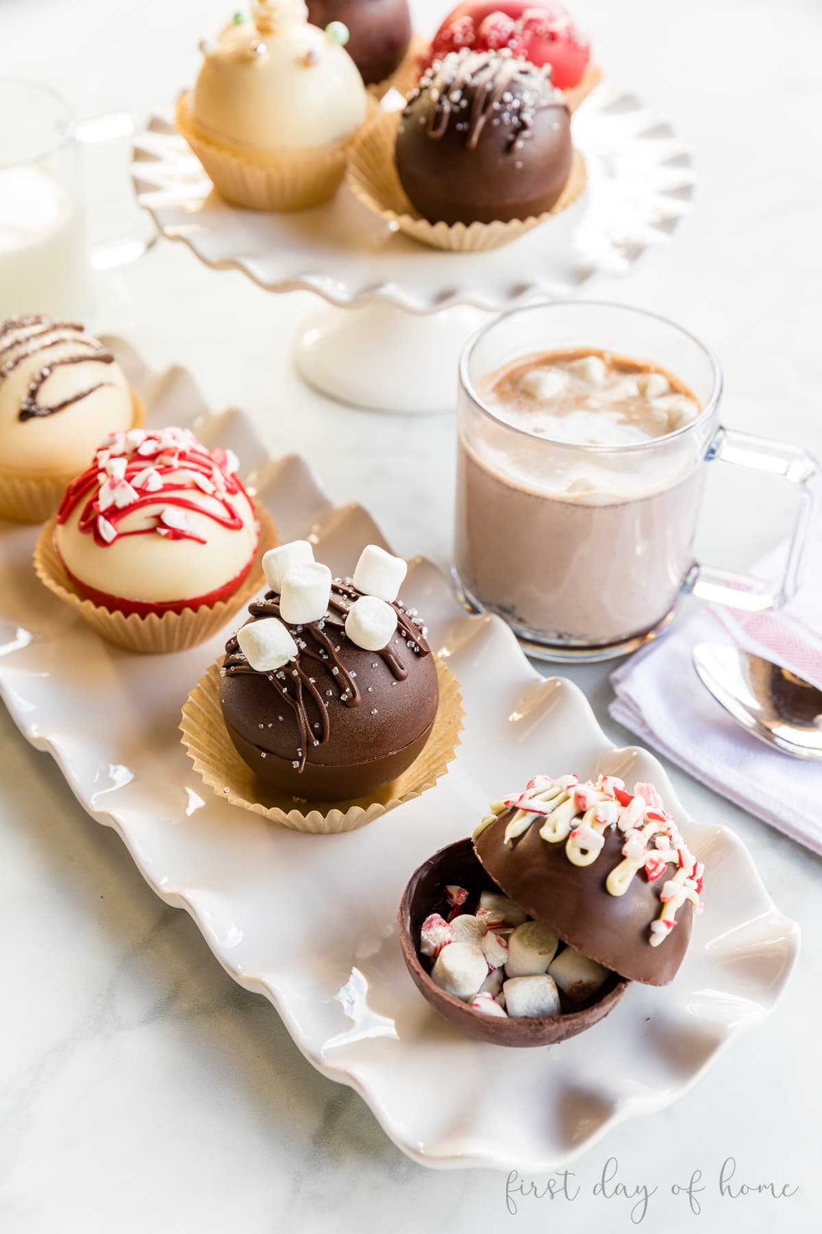 Trio of hot chocolate bombs in a tray sitting next to hot chocolate in a glass mug