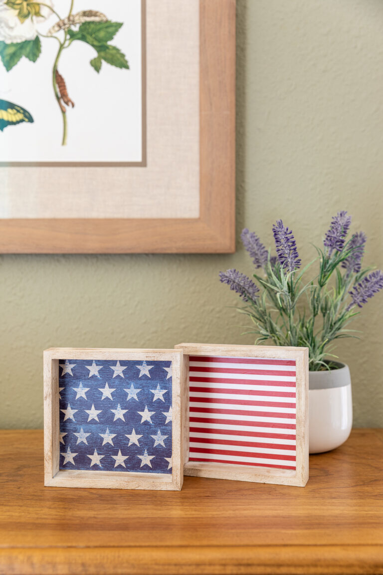 Two patriotic wood signs with stars and stripes pattern sitting next to plant on table