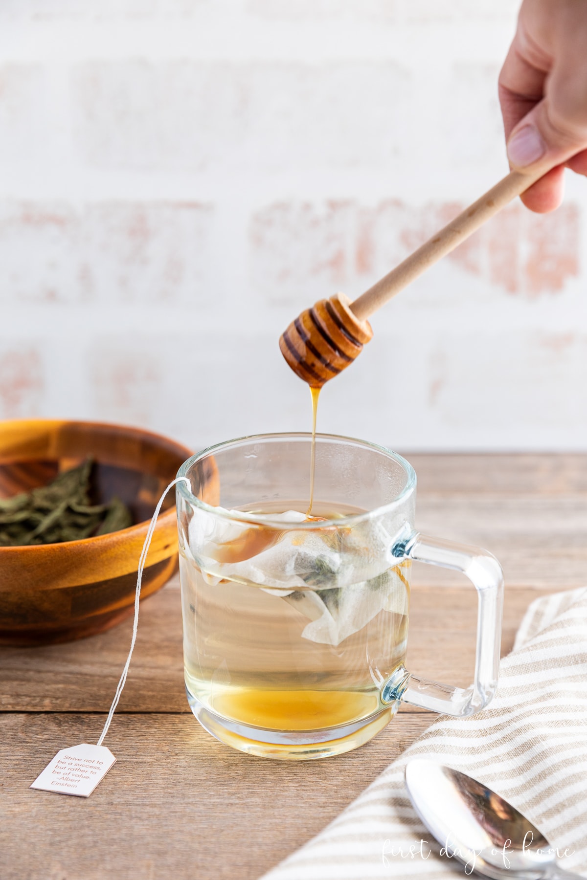Honey dipper dripping honey into mug with homemade herbal tea.
