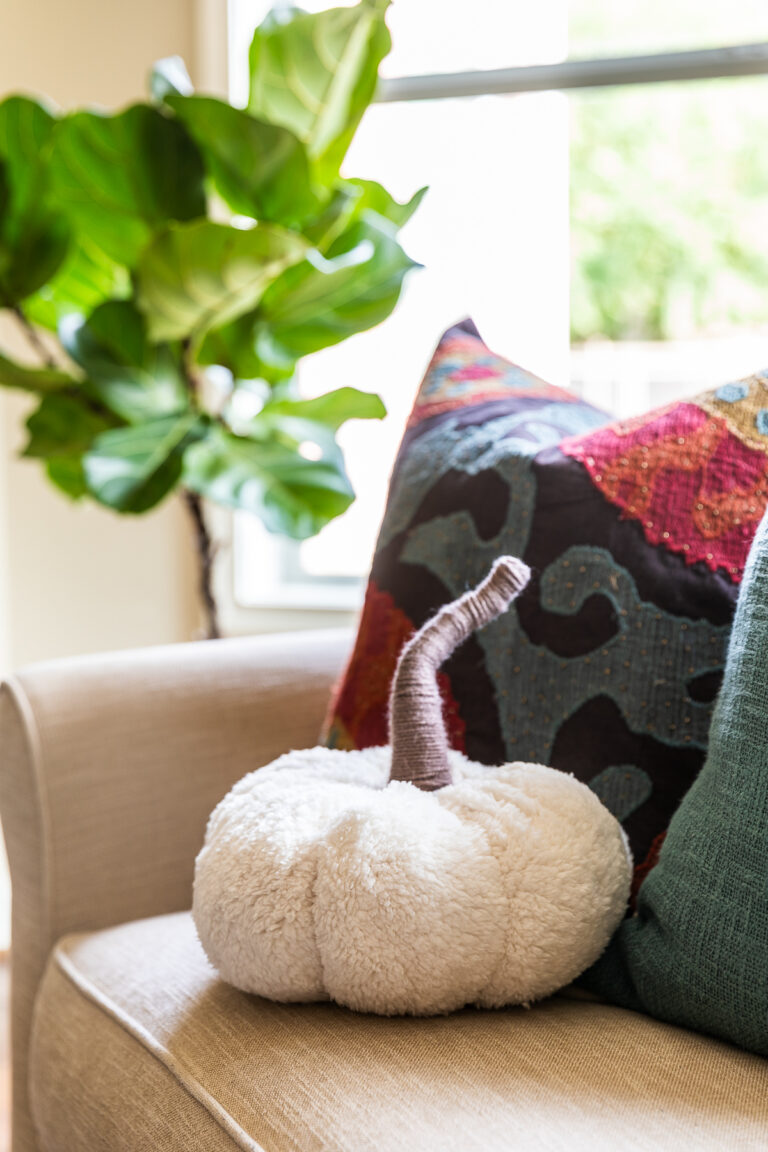 Plush DIY pumpkin pillow sitting on sofa next to throw pillows.
