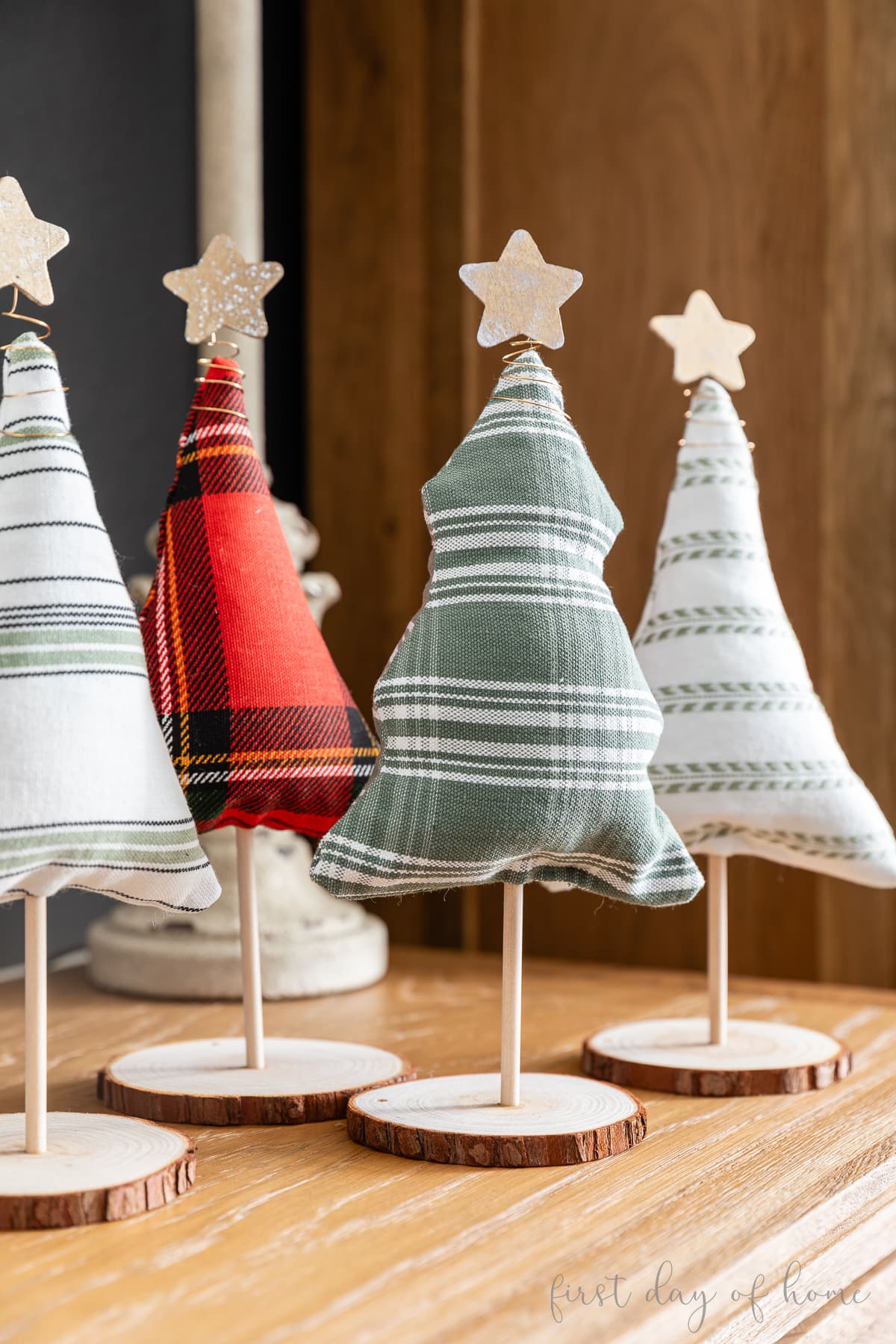 Four fabric Christmas trees on stands with wood slice bases and topped with sparkly star tree toppers.