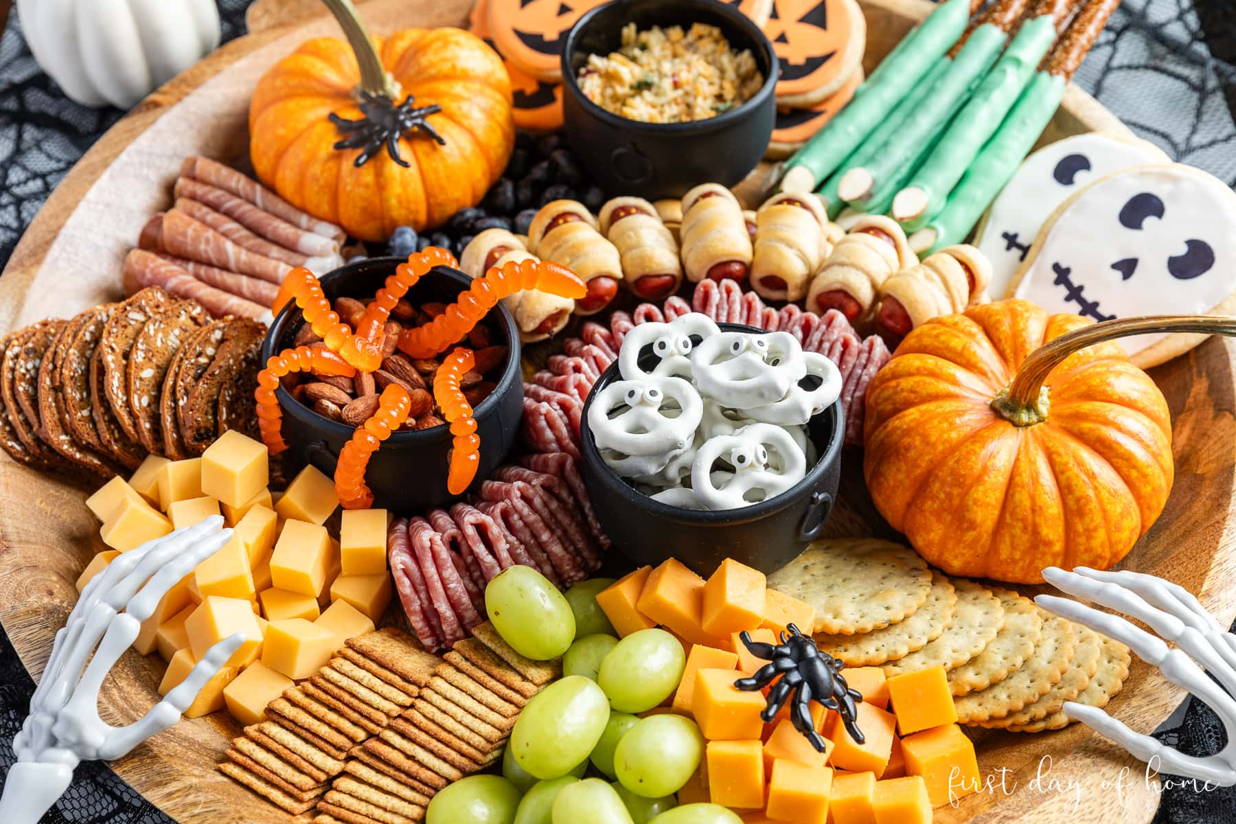 Halloween snacks on charcuterie board, including yogurt pretzels, grapes, crackers, gummy worms, cheese, and pigs in a blanket.