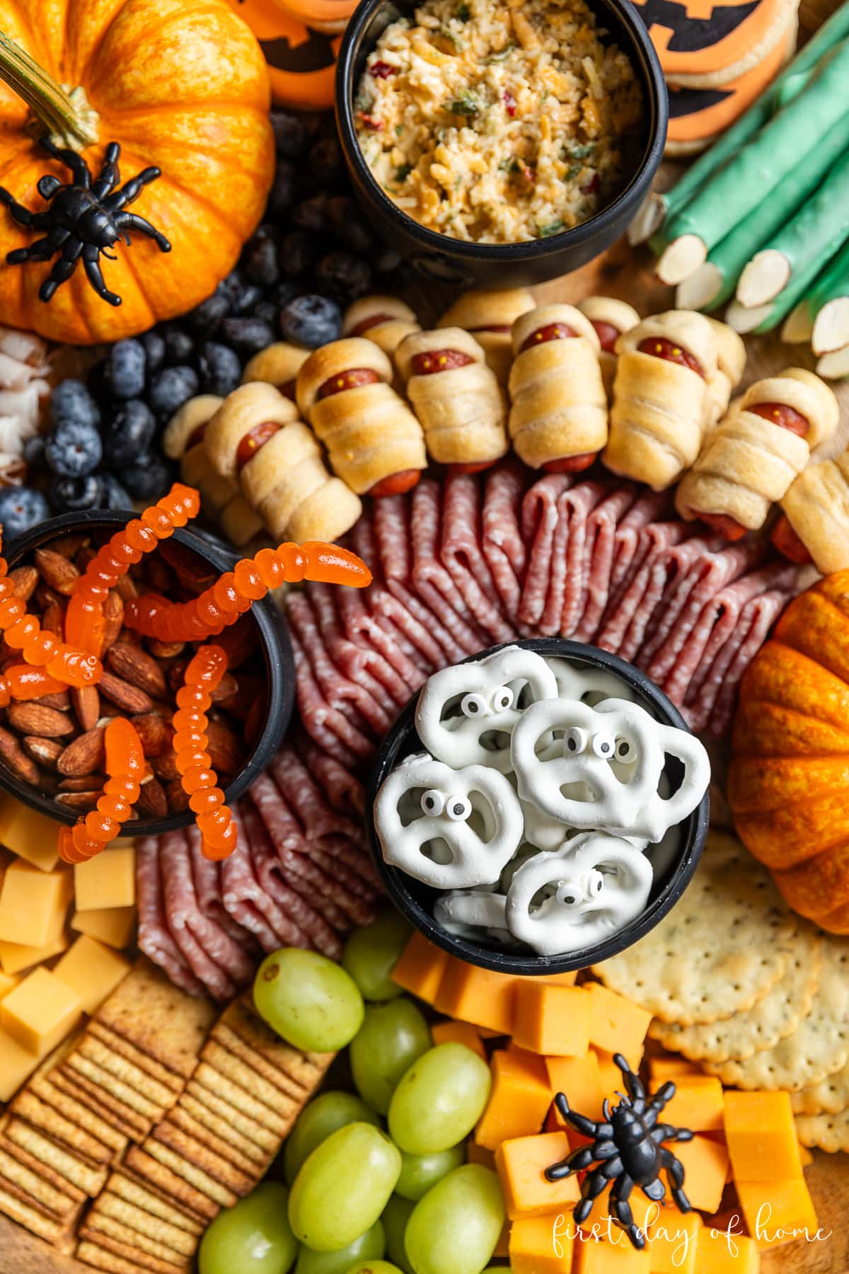 Yogurt mummy pretzel twists, salami, mummy dogs, cheese, crackers, and fruit on Halloween charcuterie board. 