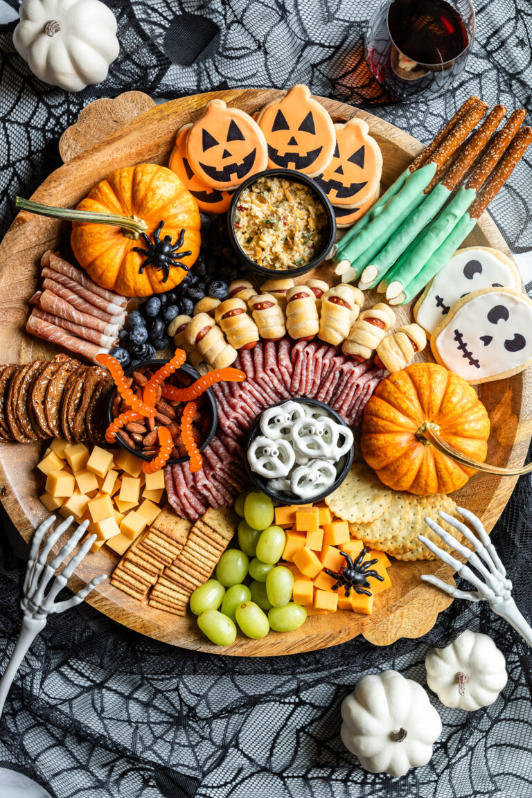 Halloween charcuterie board with crackers, meats, cheeses, grapes, blueberries, cookies, chocolate-covered pretzels, gummy worms, and other garnishes.