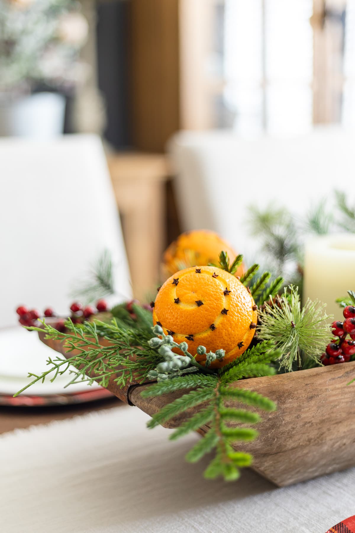 Orange pomander balls in DIY Christmas centerpiece with greenery and berries.