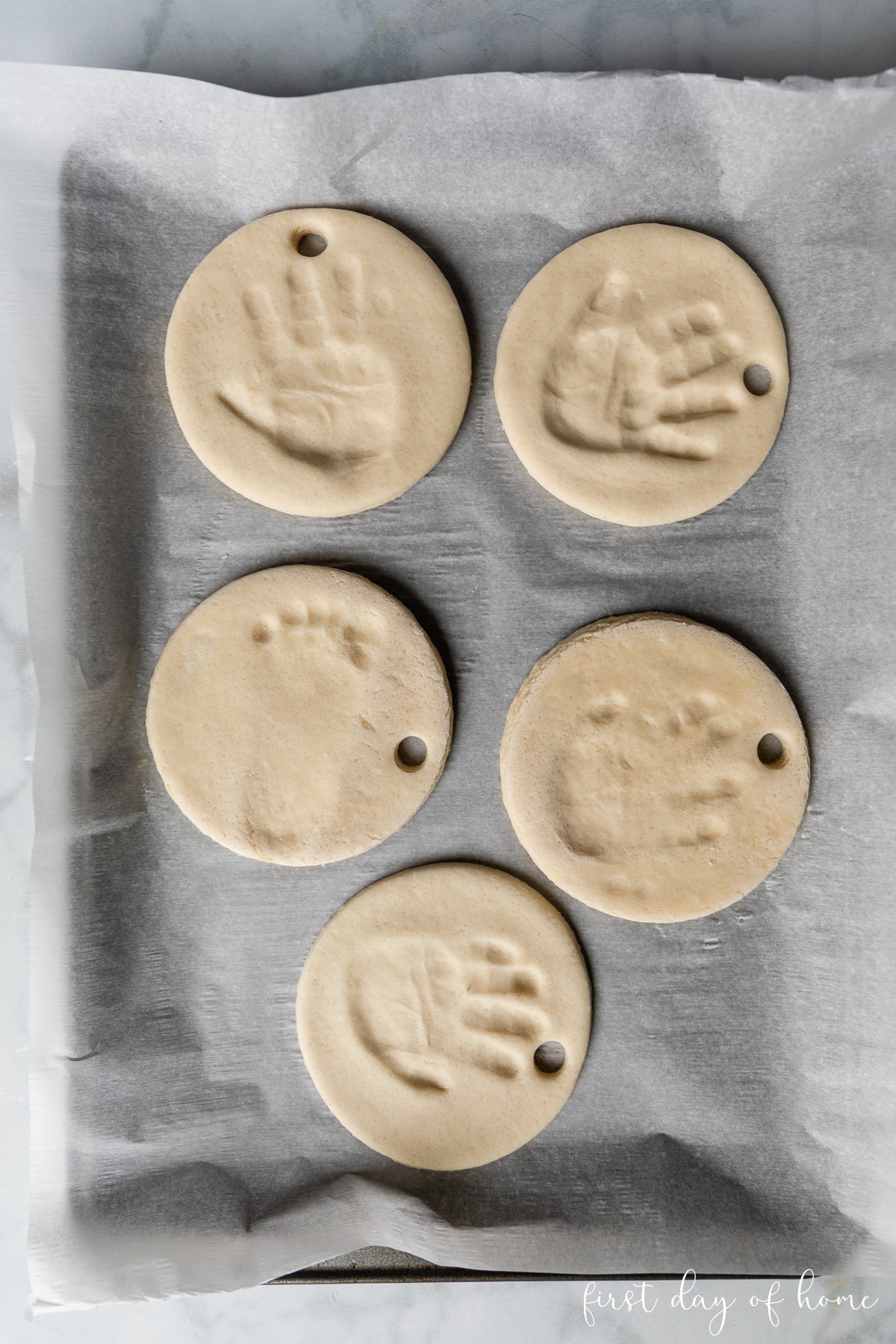 Handprints and footprints made into circular ornaments sitting on cookie sheet.