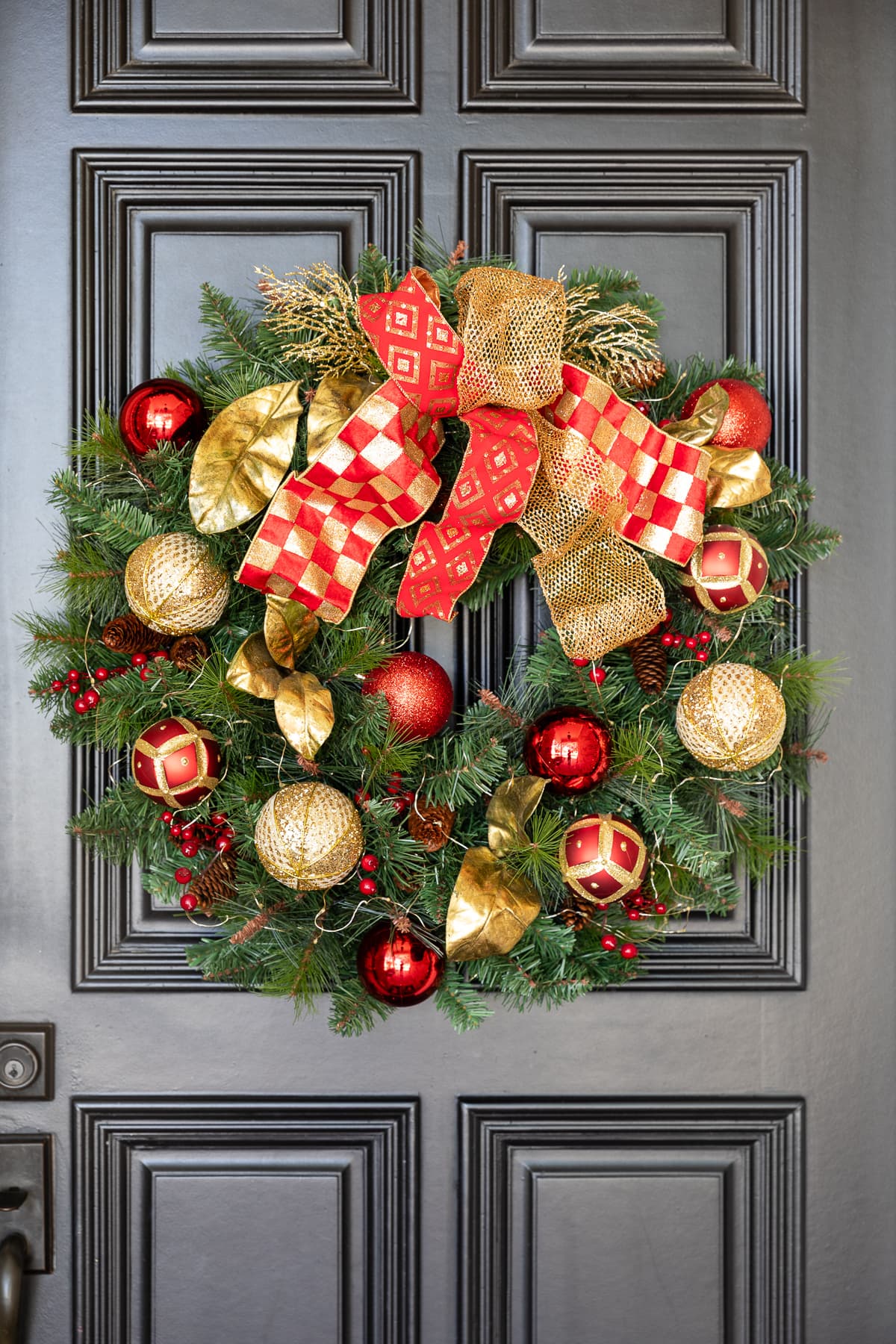 Christmas wreath decorated with red and gold ribbons, ornaments, and leaves hanging on front door.