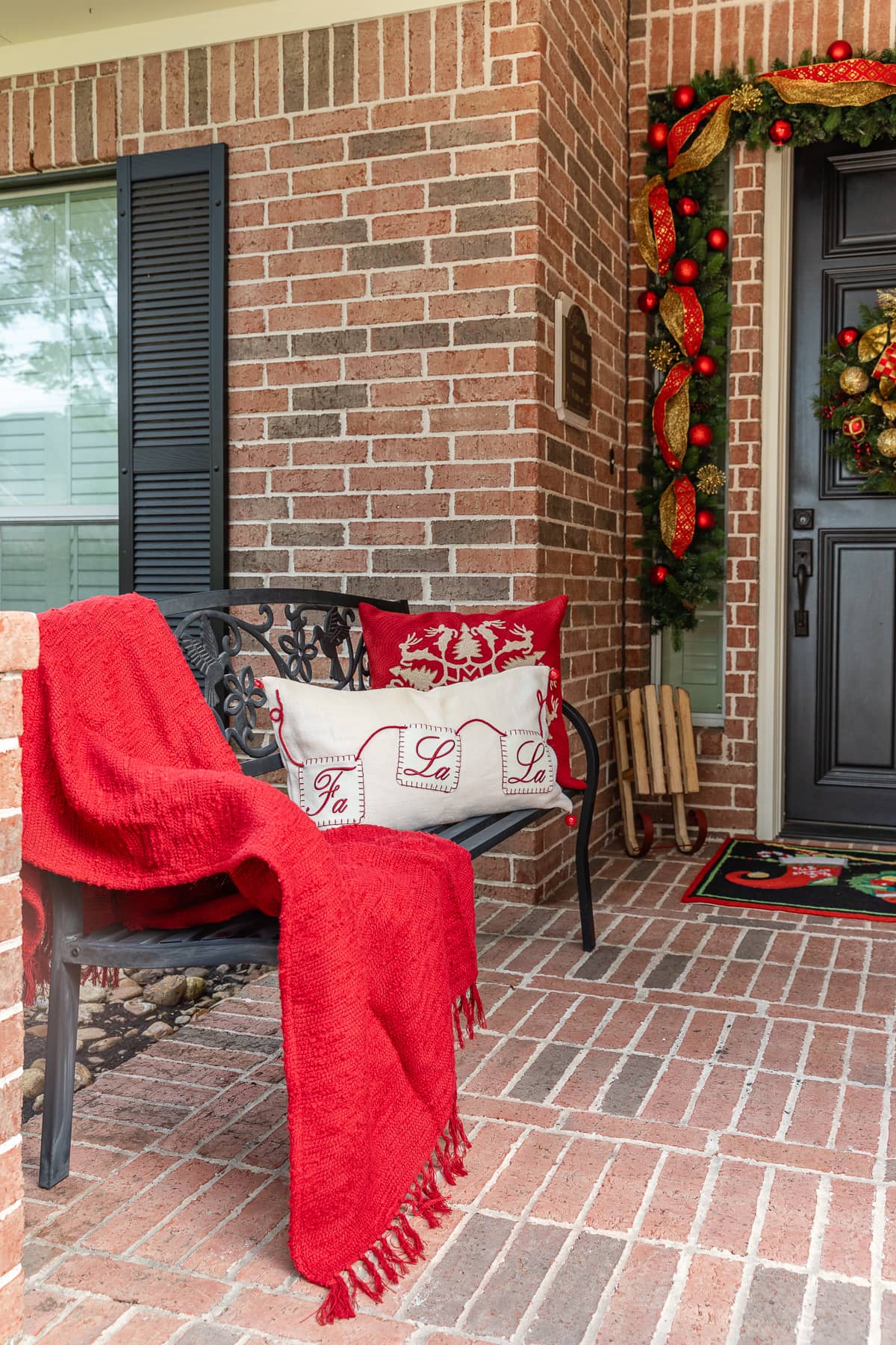 Christmas porch decorations with throw blanket and throw pillows placed on bench.