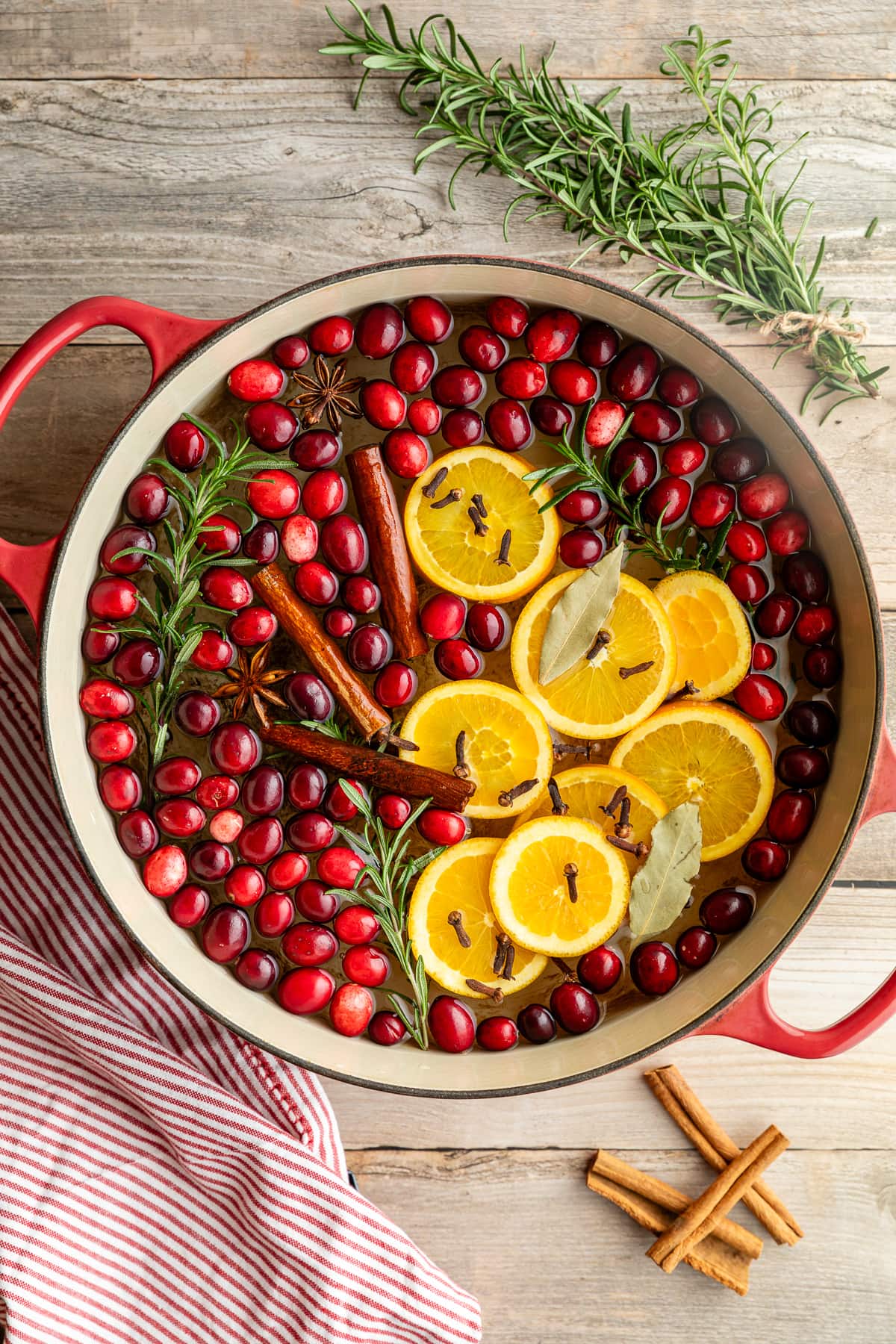 Simmer pot in Dutch oven filled with cranberries, orange slices, whole cloves, cinnamon sticks, star anise, rosemary stems, and bay leaf.