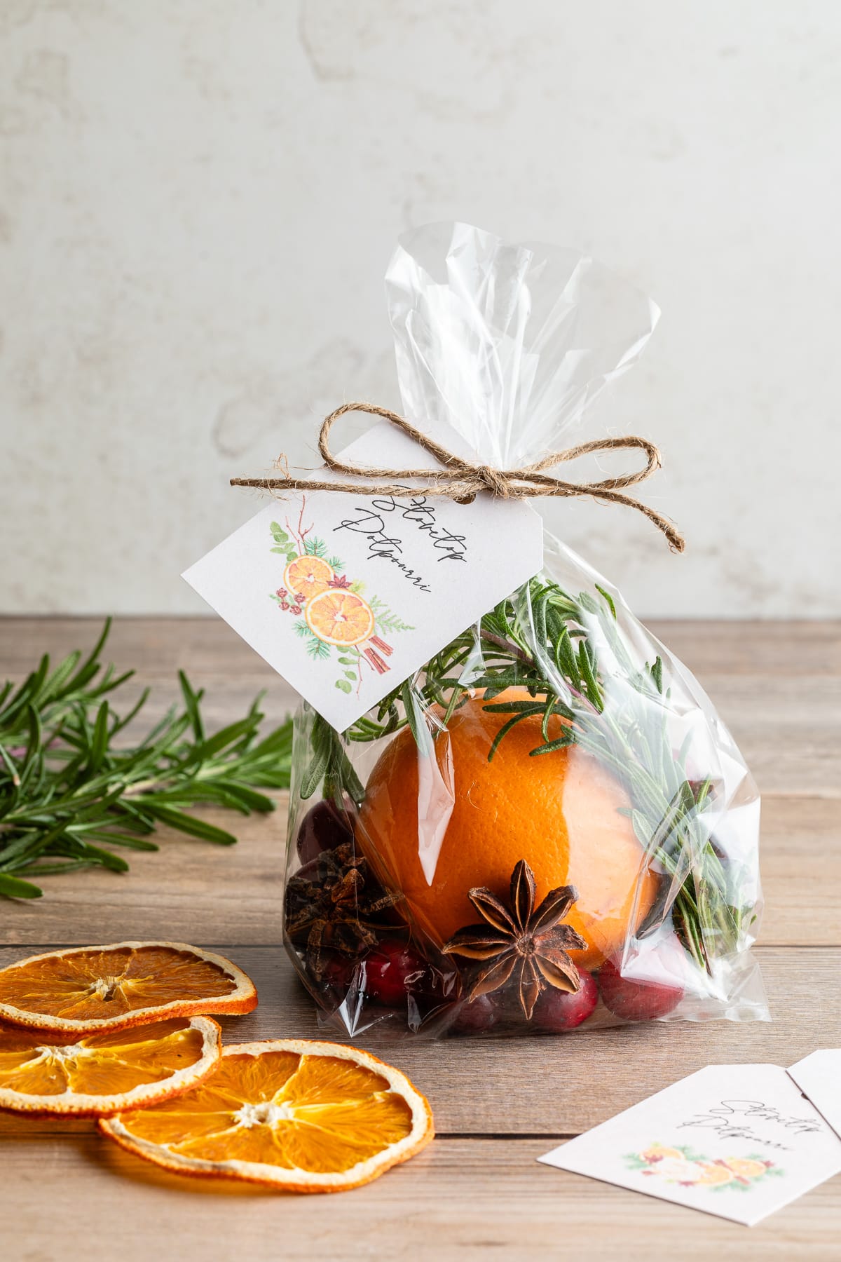 Cellophane gift bag filled with orange, cranberries, and spices shown with gift tag that says "Stovetop Potpourri" next to dried orange slices.