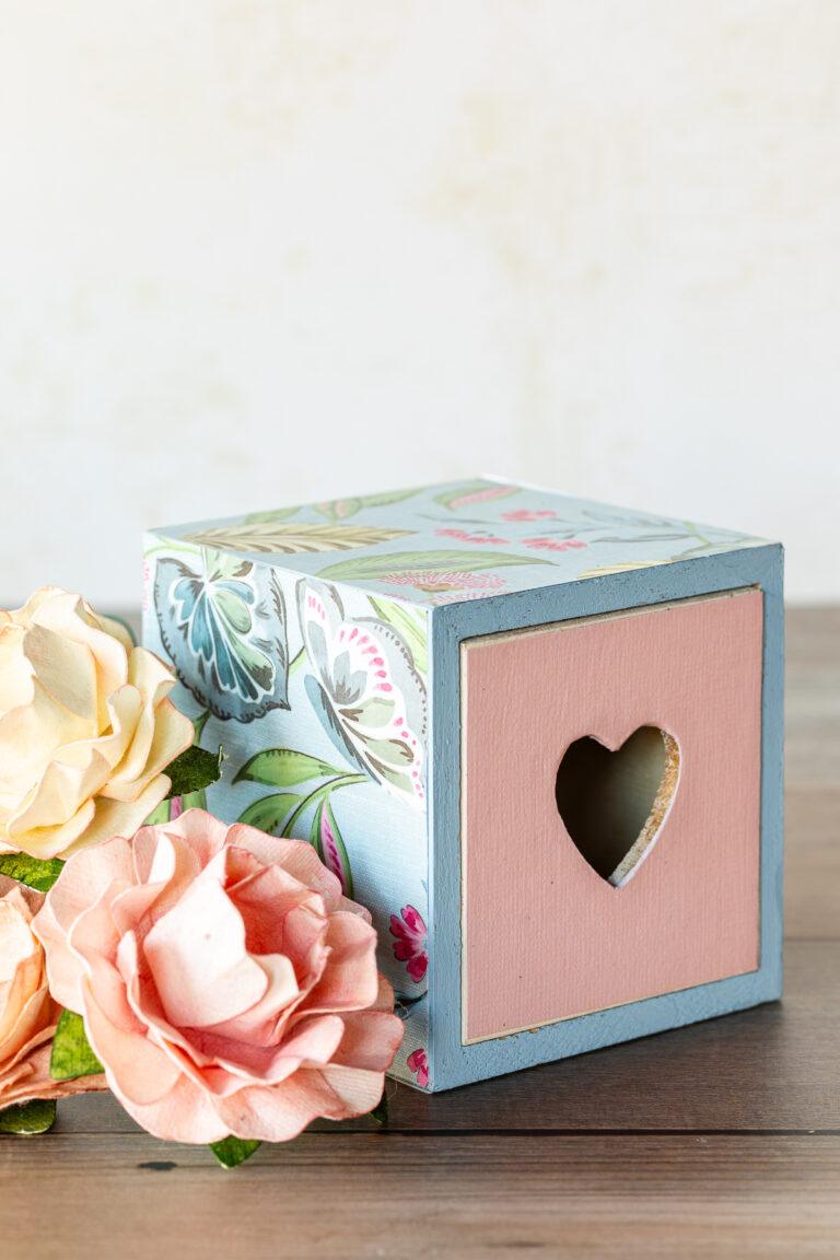 Wooden box decorated with decoupage scrapbook paper next to paper roses.
