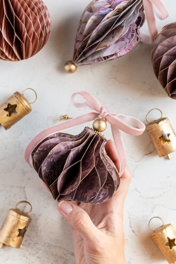 Hand holding a honeycomb paper Christmas ornament in a bulb shape.