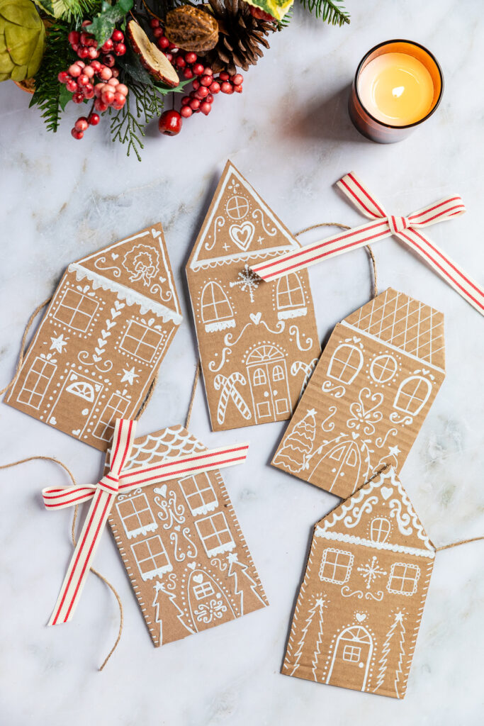 Cardboard gingerbread houses shown with a candle and greenery.
