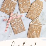 Cardboard gingerbread house garland shown with greenery and candle.