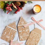 Cardboard gingerbread house garland shown with greenery and candle.