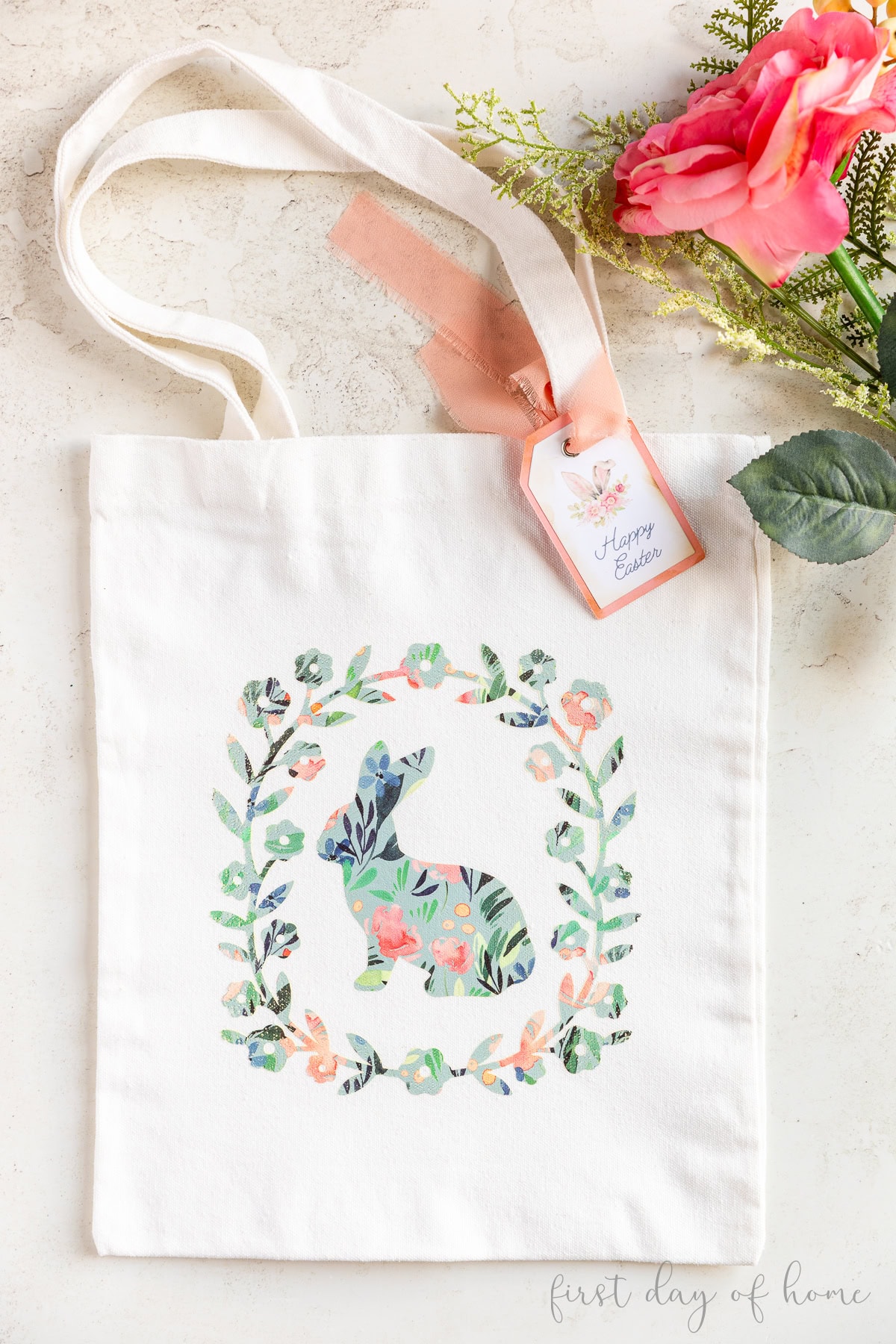 Tote bag with patterned vinyl design of bunny and wreath, shown with flowers.