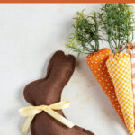 Brown felt bunny with yellow ribbon around its neck, shown with fabric carrots.