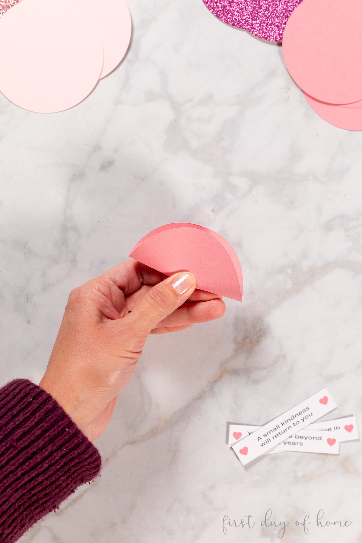 Creasing a paper circle in the middle to create a fortune cookie shape.
