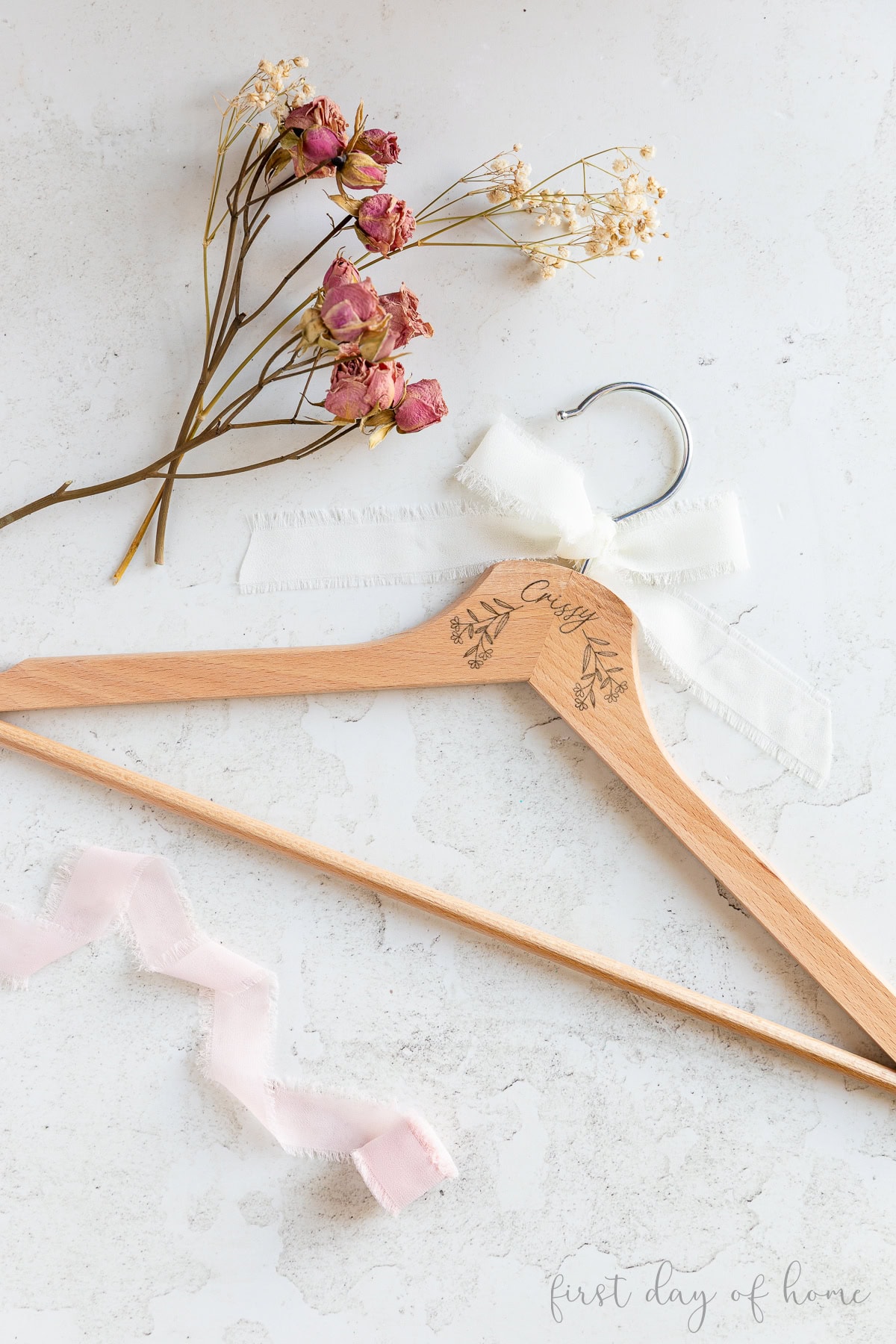 Wooden hanger laser engraved with a name and flowers, shown with dried flowers and ribbon.