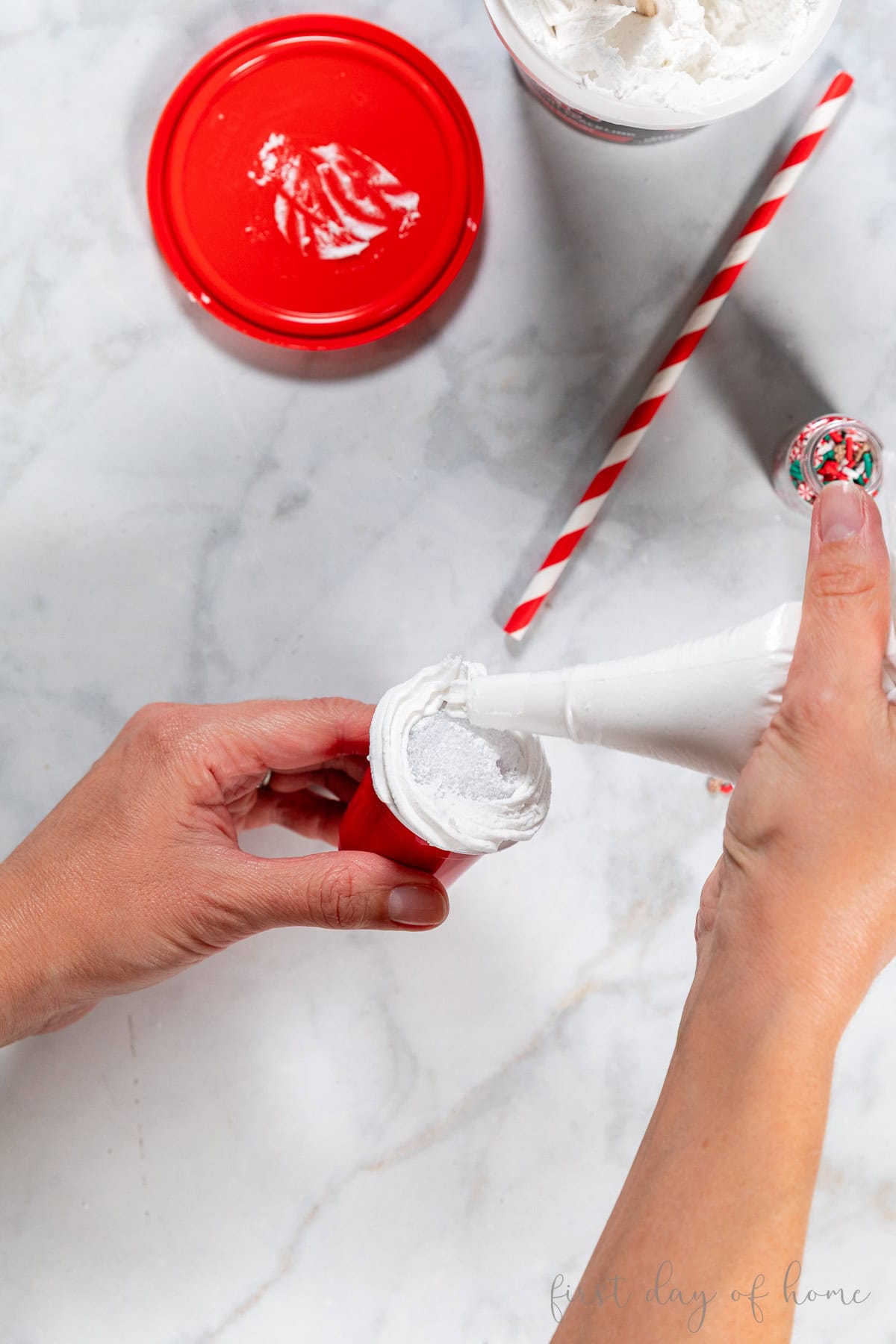 Adding spackling around a styrofoam ball inside a mini cup using a frosting piping bag.