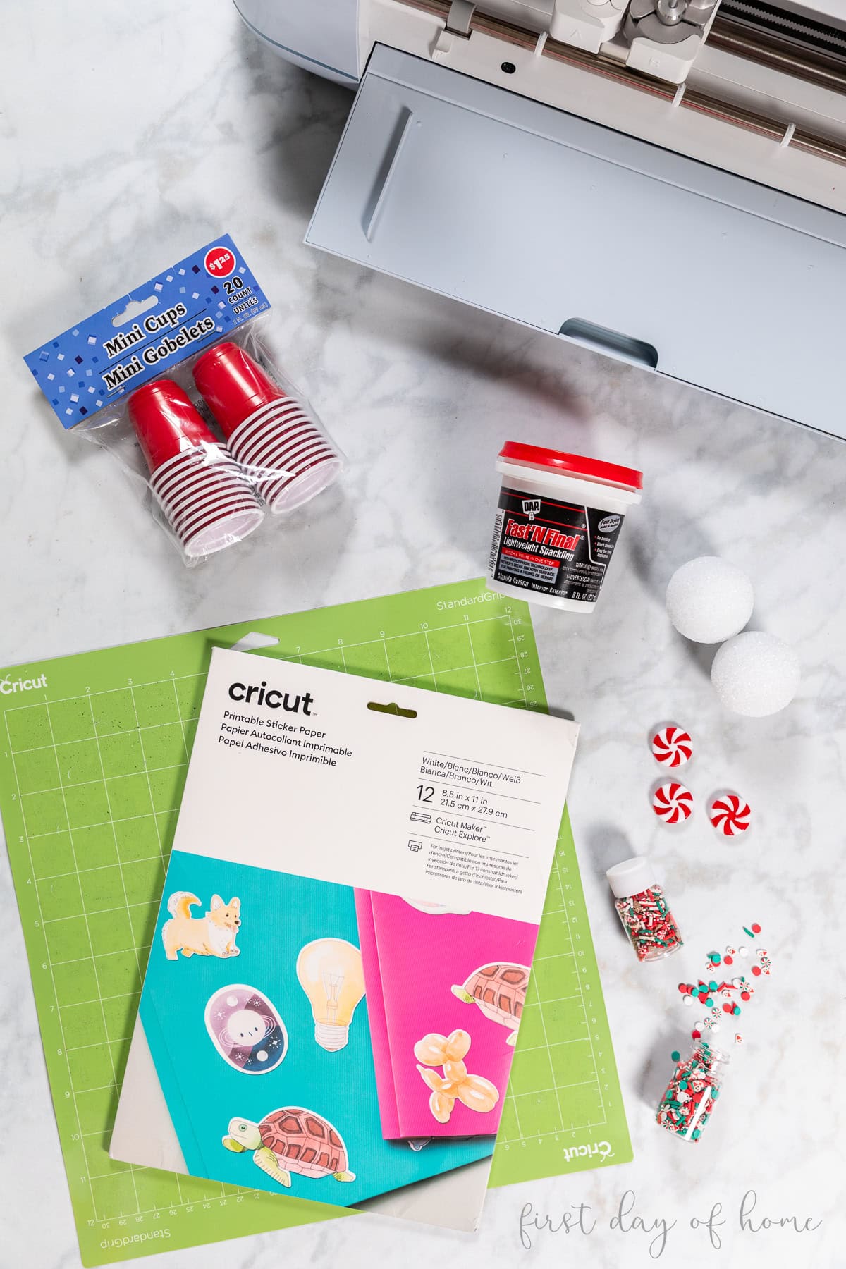Supplies for making mini coffee cup ornaments, including small shot glass cups, spackle, faux sprinkles, and Cricut sticker supplies.