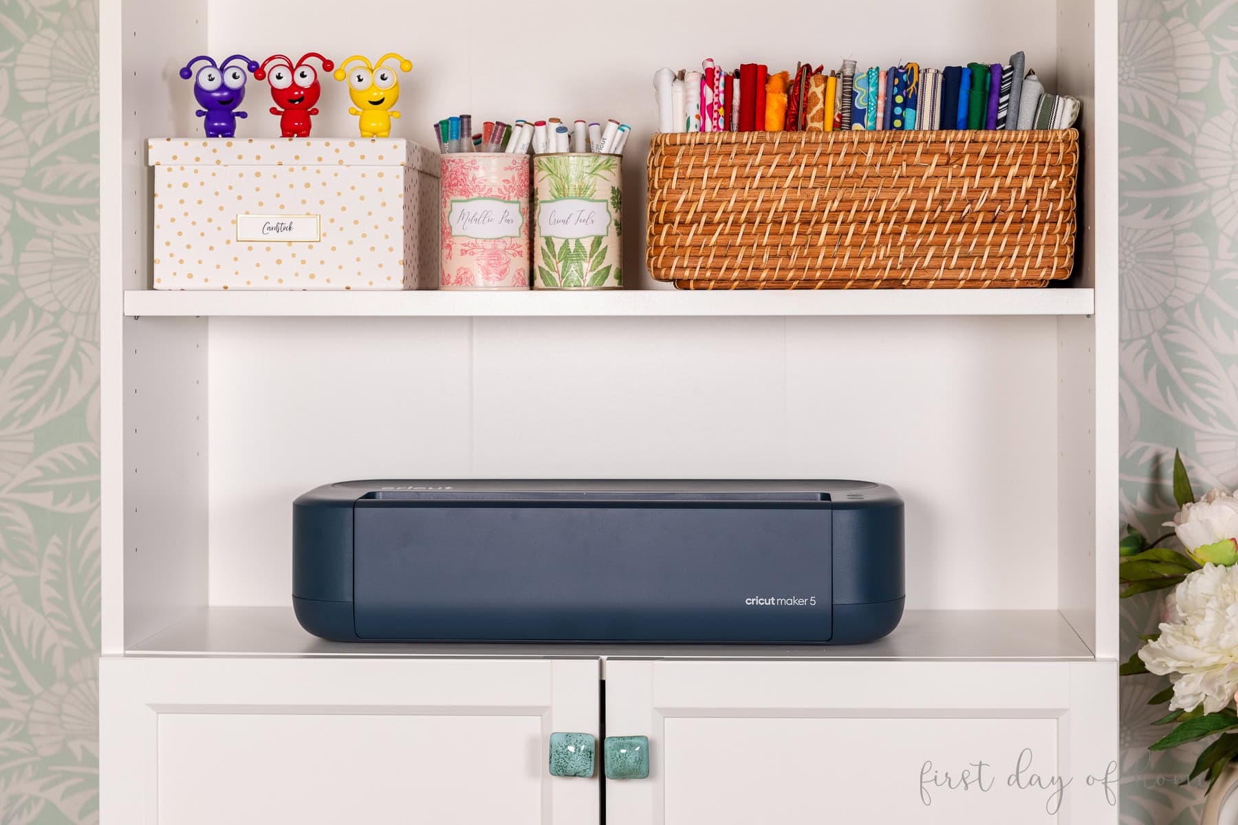 Cricut Maker 5 sitting on a bookcase with other craft supplies.