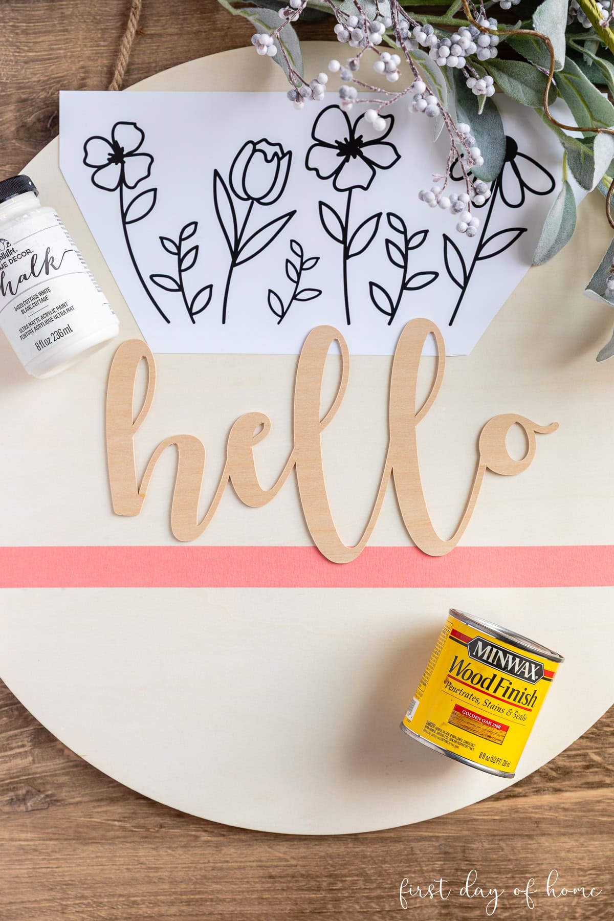 Unfinished wood round with phrase "hello" and vinyl flowers before painting and assembling into a DIY wooden door hanger.